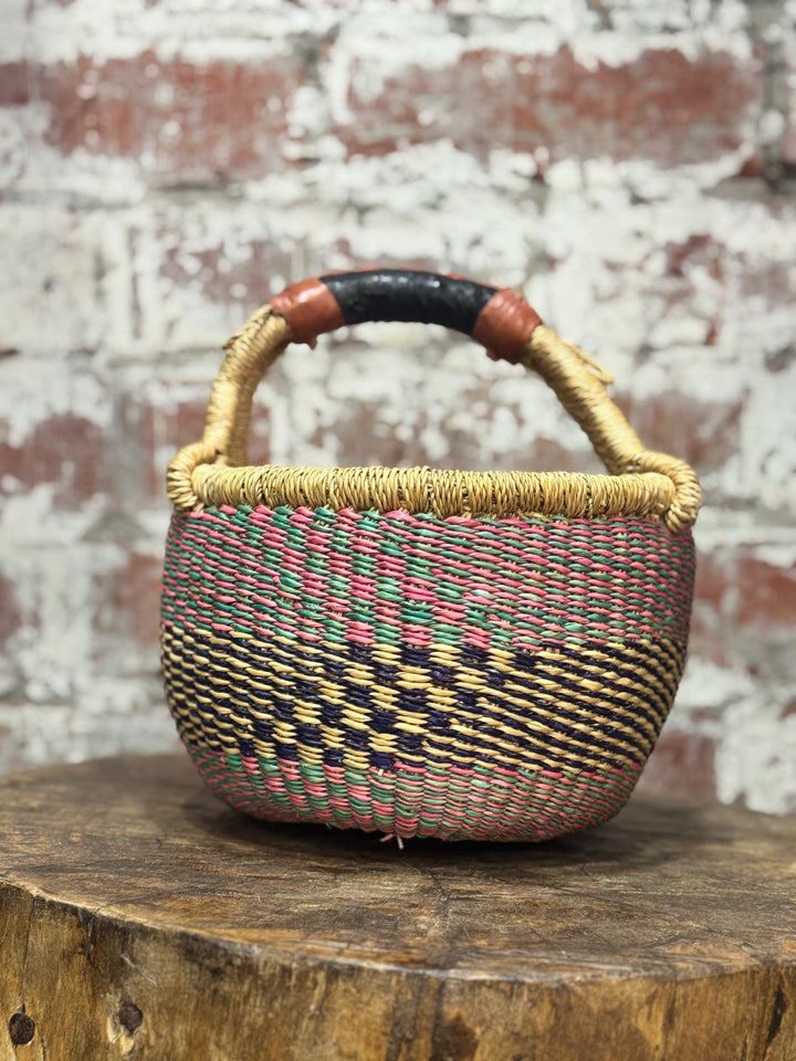 Woven basket with a colorful handle on a wooden surface with a brick wall background