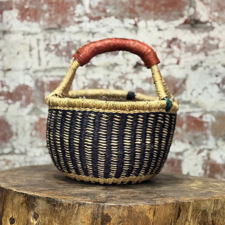 Woven basket with a red handle on a wooden surface against a brick wall.