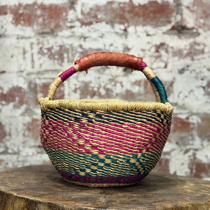 Woven basket with colorful handle on a wooden surface against a brick wall background