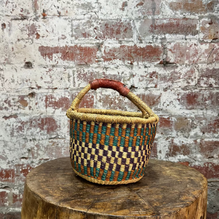 Woven basket with a checkered pattern on a wooden stump against a brick wall.