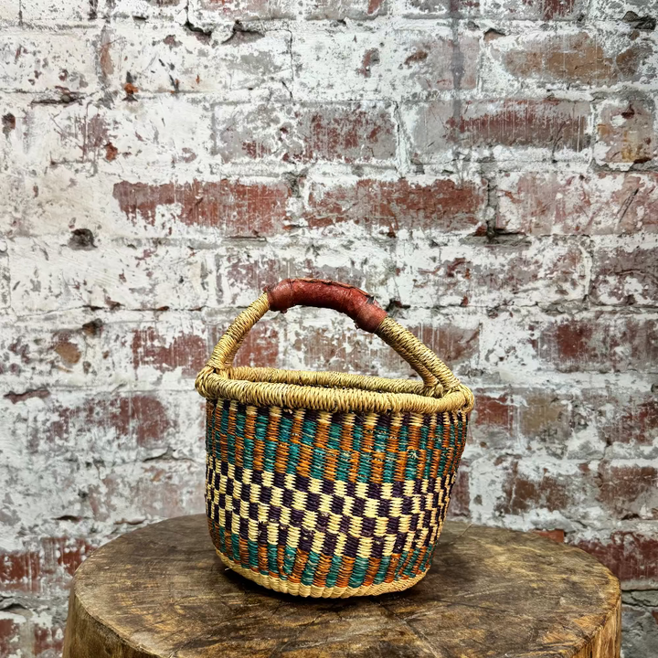 Woven basket with a checkered pattern on a wooden stump against a brick wall.