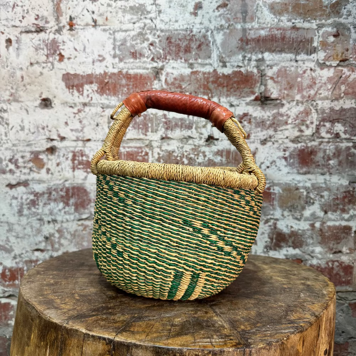 Woven basket with a red handle on a wooden stump against a textured brick wall.