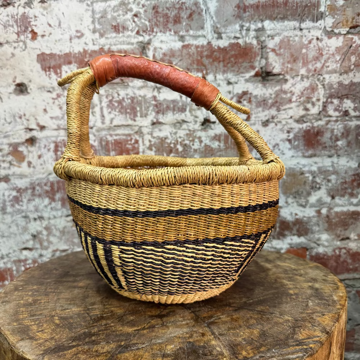 Woven basket with a handle on a wooden surface against a brick wall background