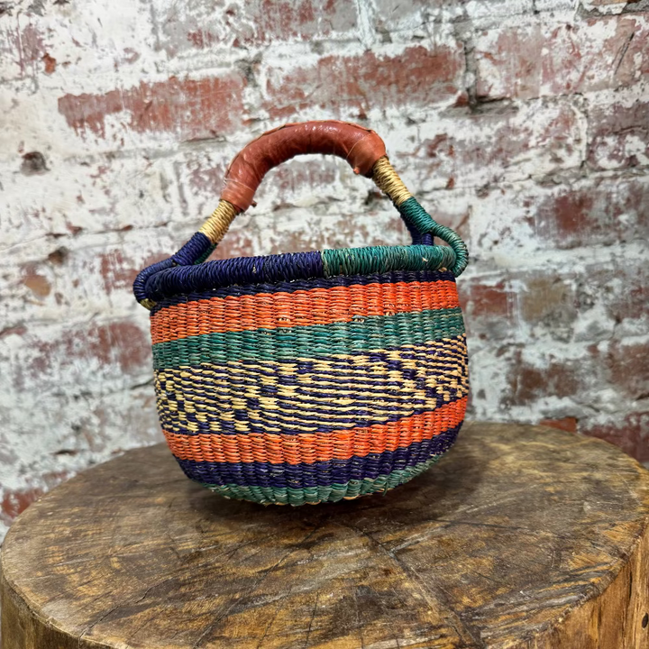 Woven basket with colorful handle on a wooden stump against a textured brick wall.