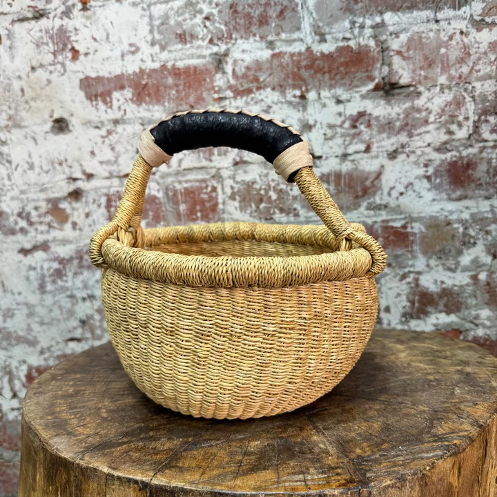 Woven basket with a black handle on a wooden stump against a brick wall.