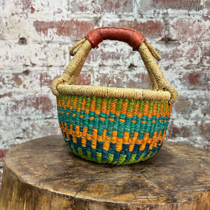 Woven basket with a colorful pattern on a wooden stump against a brick wall.