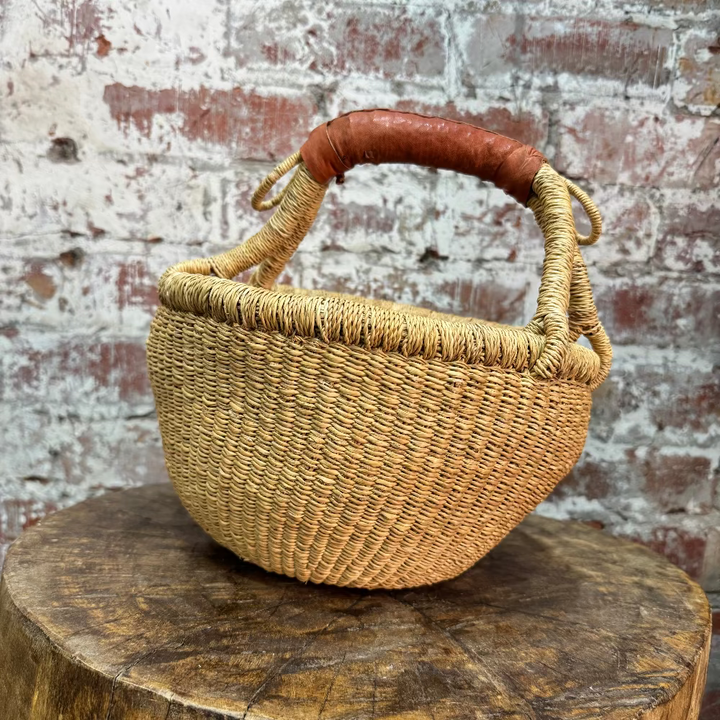 Woven basket with a brown handle on a wooden stump against a brick wall.