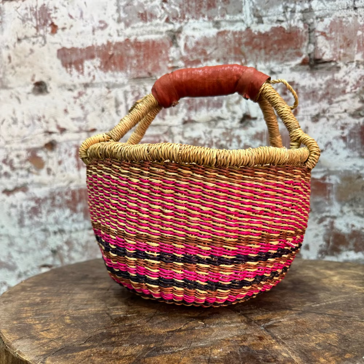 Woven basket with a colorful handle on a wooden surface with a brick wall background