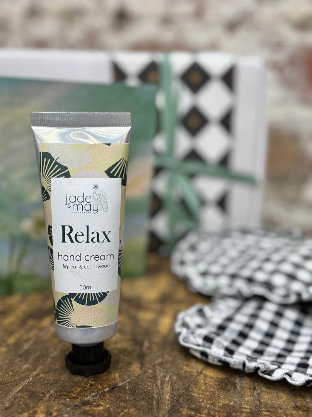 Hand cream tube labeled 'Jade May Relax' on a wooden surface with a blurred background