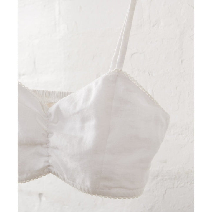 White Bralette in Linen-Jade and May-Bralette- Everyday Essentials- Close up of bralette shown hanging against a white wall