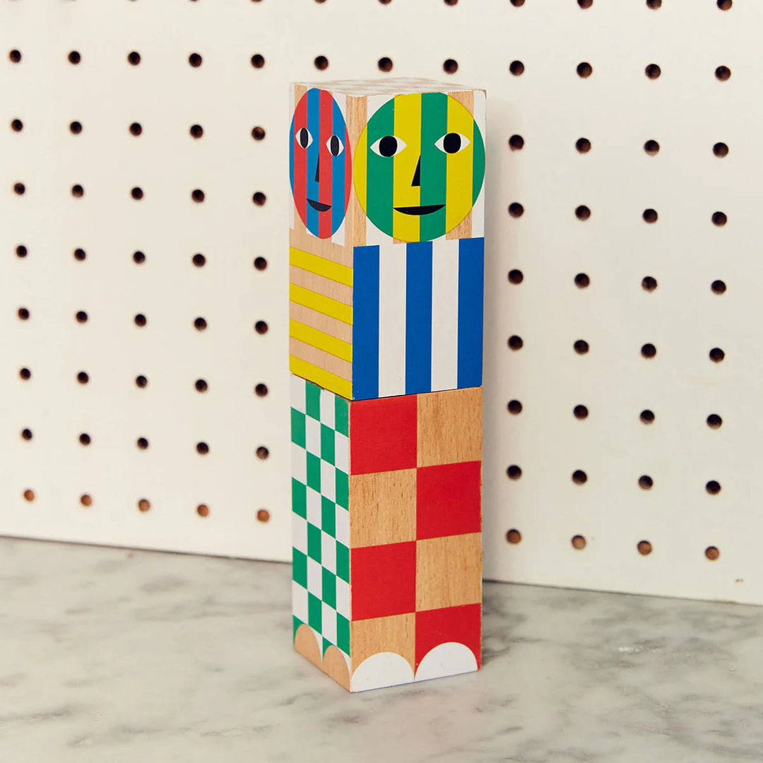 Colorful wooden block sculpture with abstract faces on a pegboard background