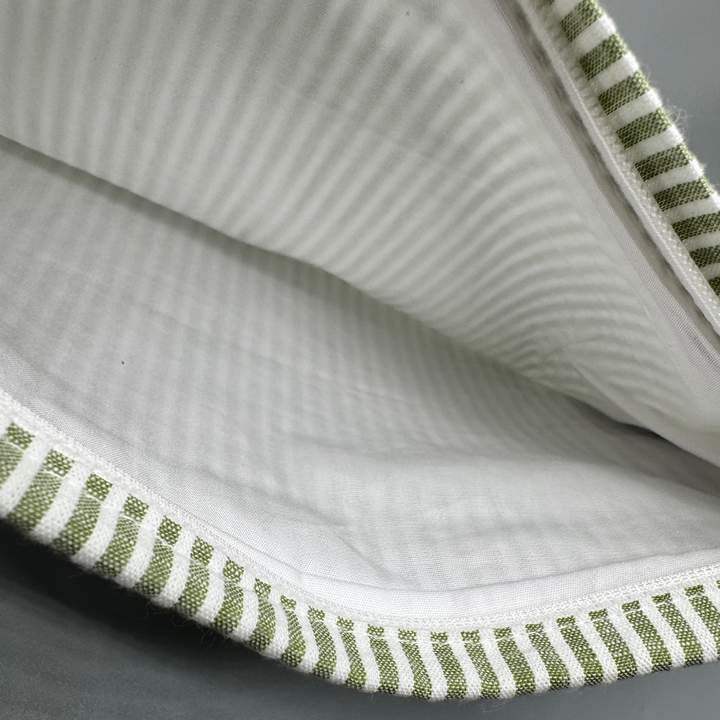 Close-up of a fabric with green and white striped trim on a gray background