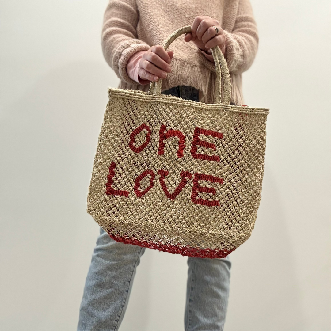 Person holding a woven bag with 'ONE LOVE' text against a plain background