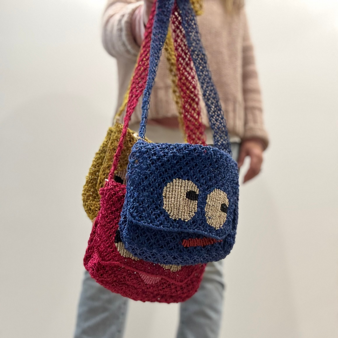Person holding a blue knitted bag with a face design against a plain background