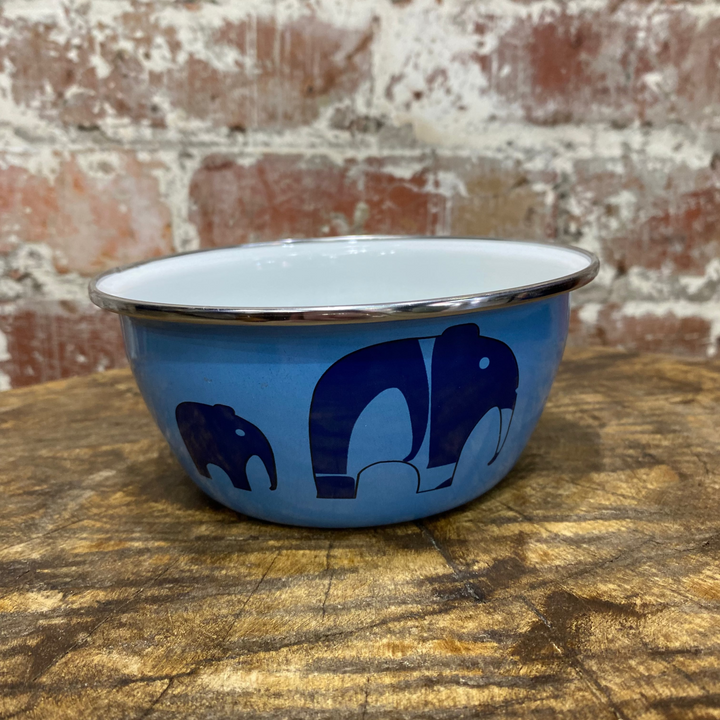 Blue enamel bowl with elephant design on a wooden surface and brick wall background