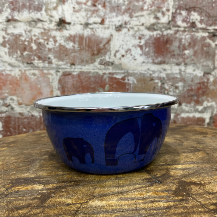 Blue enamel bowl with white interior on a wooden surface against a brick wall.