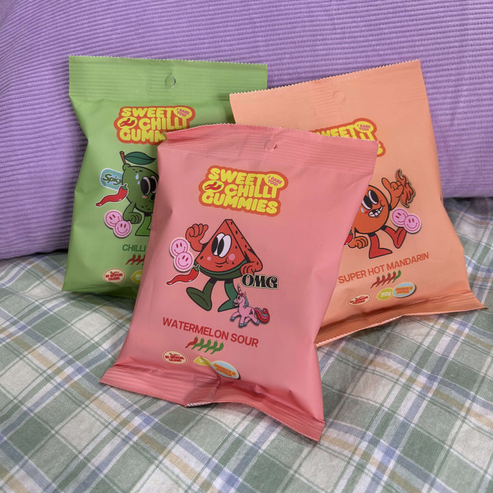 Three colorful packages of 'Sweet & Chilly Gummies' on a checkered surface with a purple background.