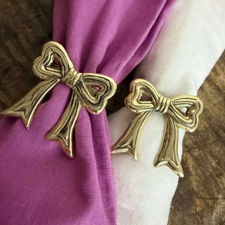 Gold bow-shaped napkin holders on purple and white fabric