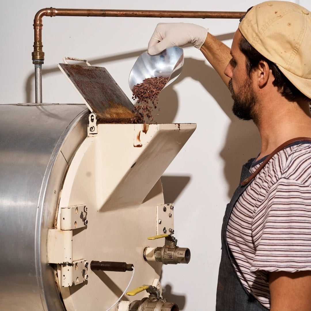 Person operating a large metal machine, likely a coffee roaster, with a white background.
