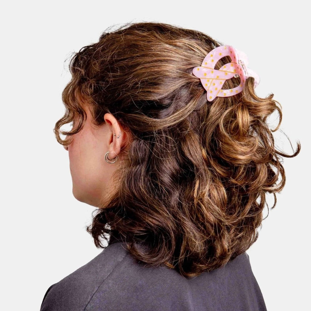 Person with styled hair featuring a pink hair clip on a plain background