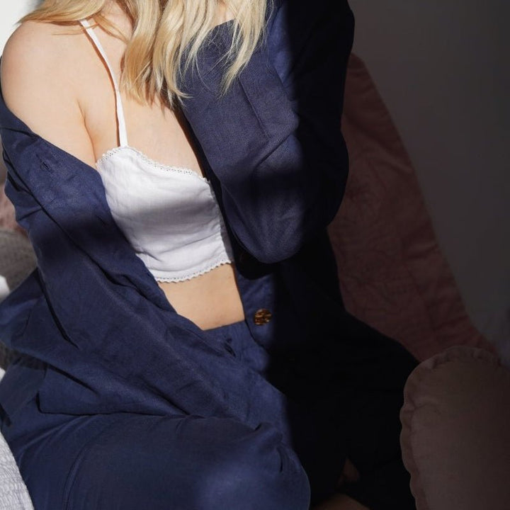 Person wearing a navy linen pyjamas over a white top sitting on a couch.
