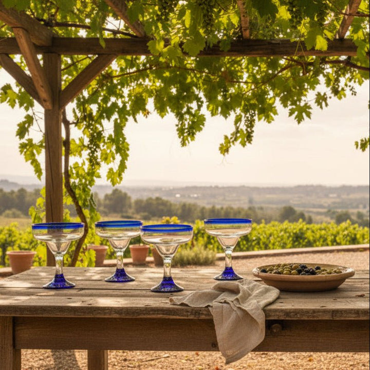 Cocktail glass with blue rim and base on a wooden surface against a rustic brick wall.