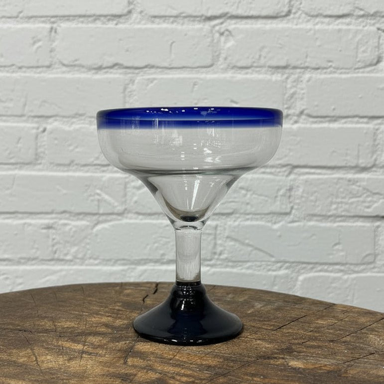 Clear glass with blue rim on a wooden surface against a white brick wall