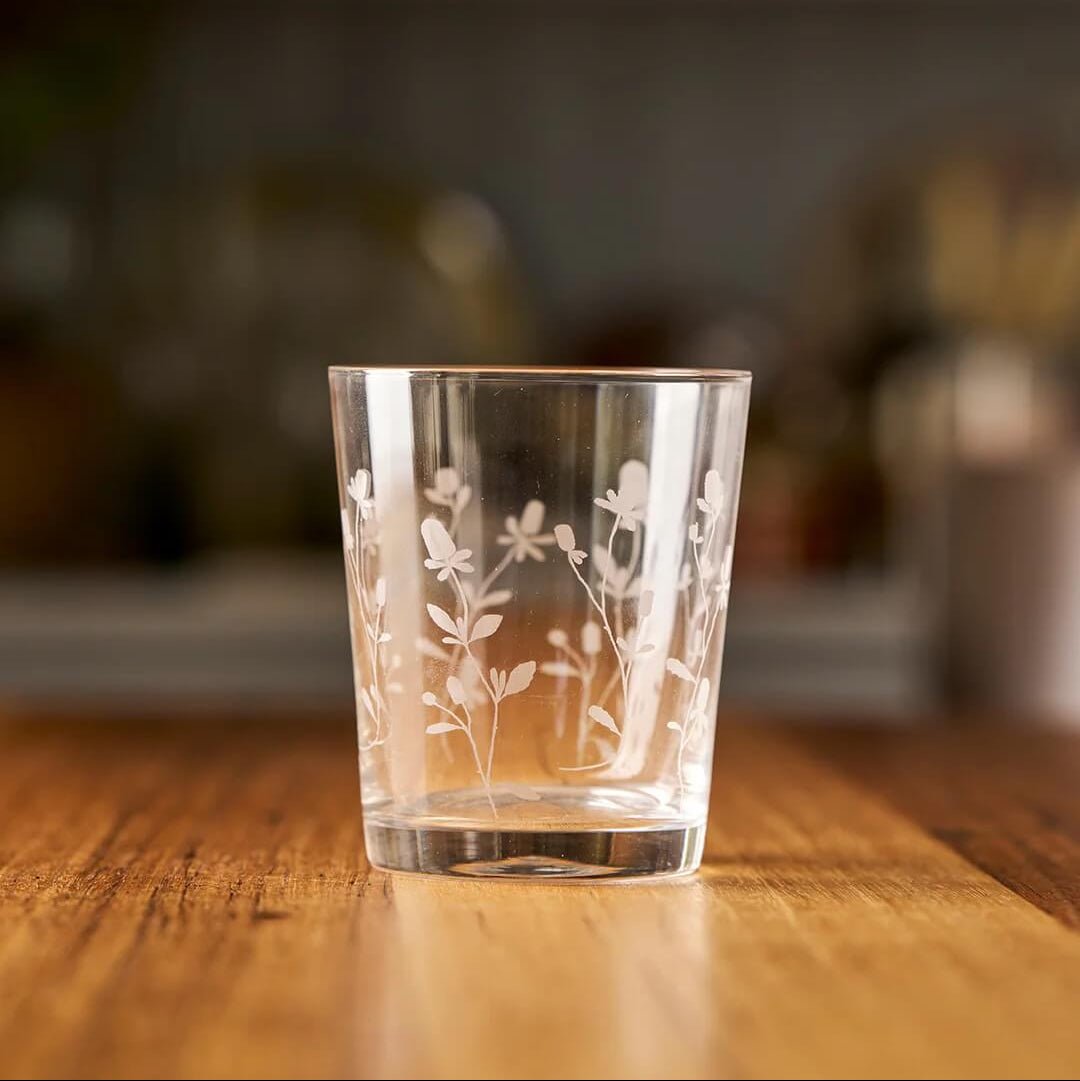Clear glass with floral etching on a wooden surface